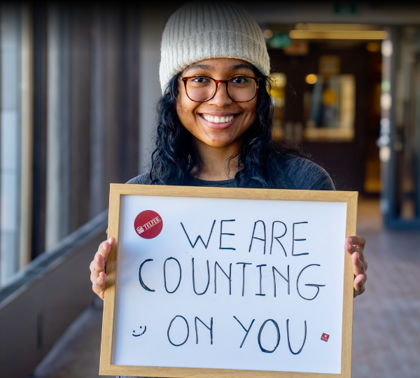 Élève tenant un tableau blanc avec le texte « We are counting on you » (Nous comptons sur vous)
