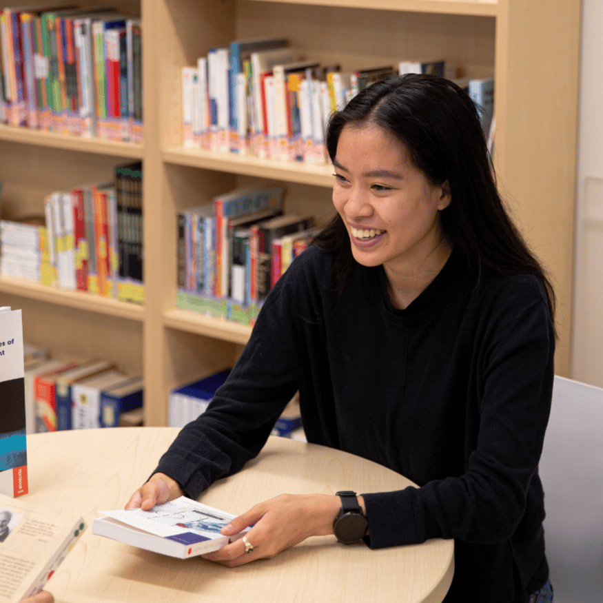Étudiante ou étudiant souriant en train de tenir un livre.