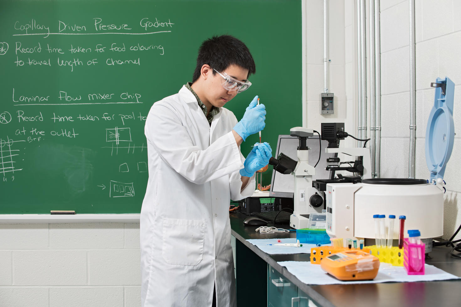 student in lab coat in lab using test tube and microscope