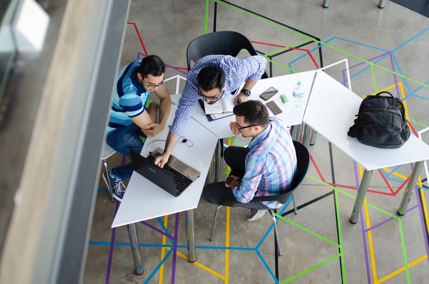 overhead view of three student workers collaborating in modern space with multicoloured lines on floor