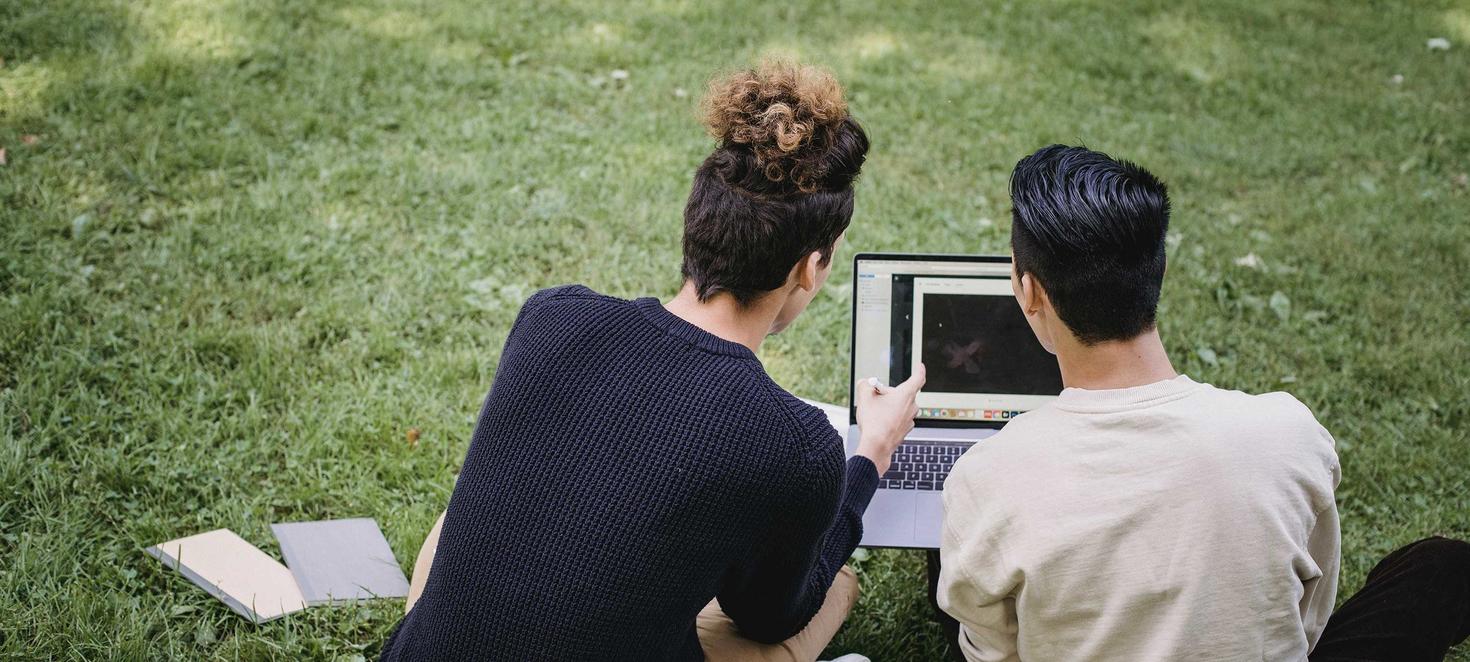 Students looking at a computer on a lawn