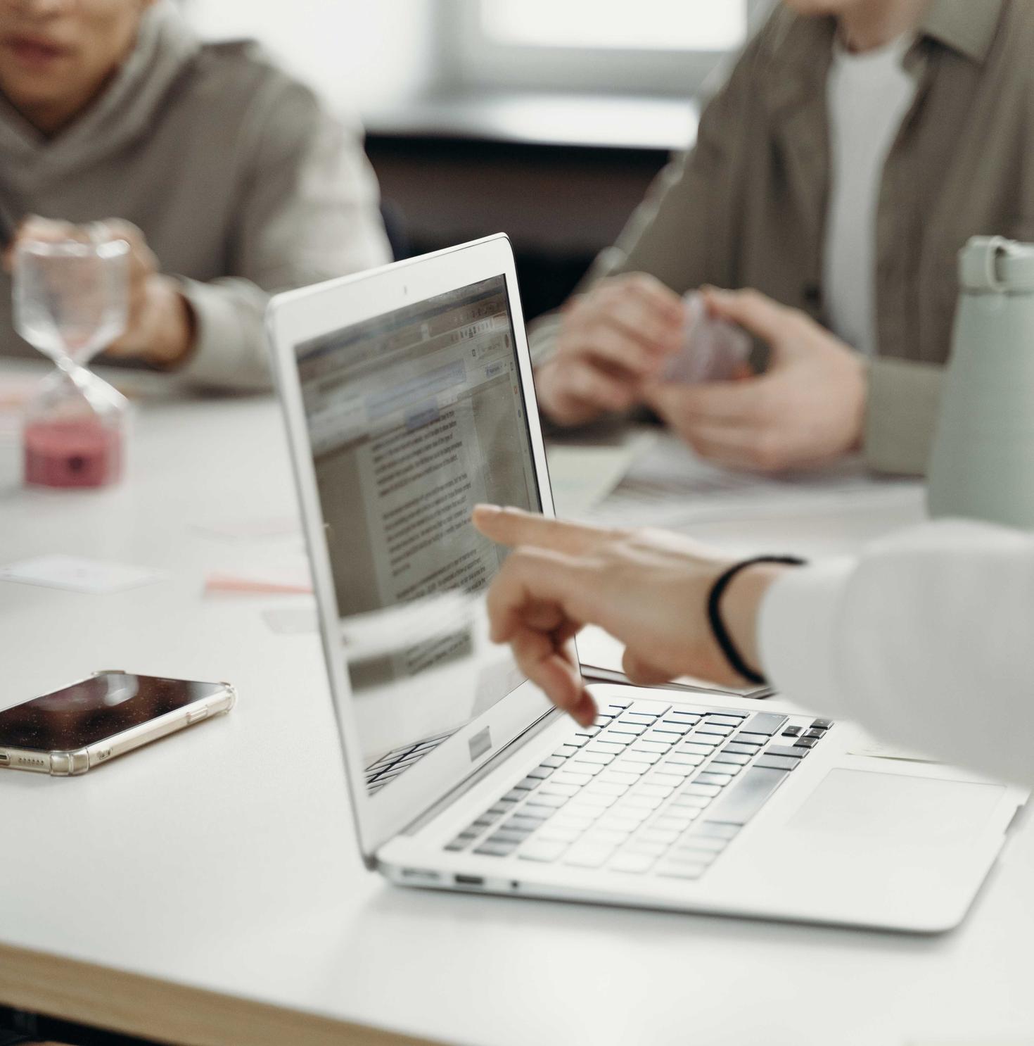 Main pointant à un écran d'ordinateur portable sur une table entourée de gens