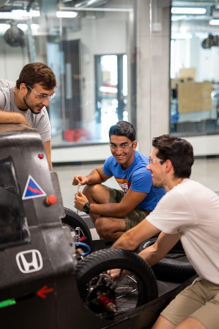 Trois membres de la communauté étudiante portant des lunettes de protection travaillent sur une voiture électrique.