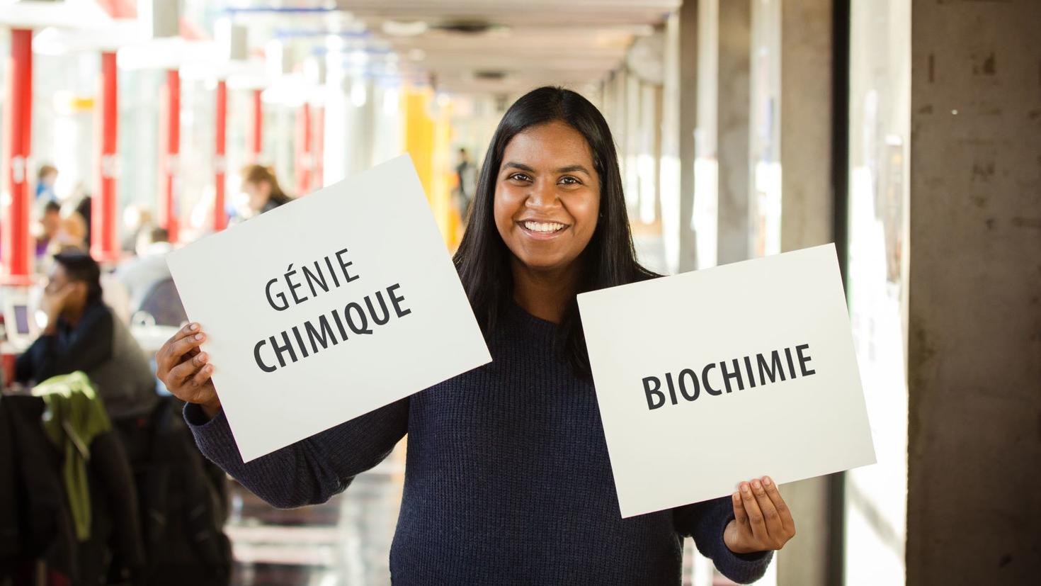 Un étudiant heureux tenant deux panneaux indiquant "Génie chimique et biochimie"