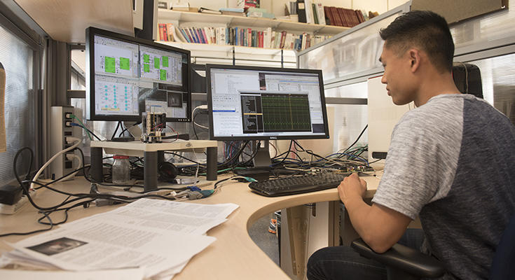 Un étudiant assis devant deux écrans d’ordinateur, où l’on peut voir plusieurs fichiers ouverts.