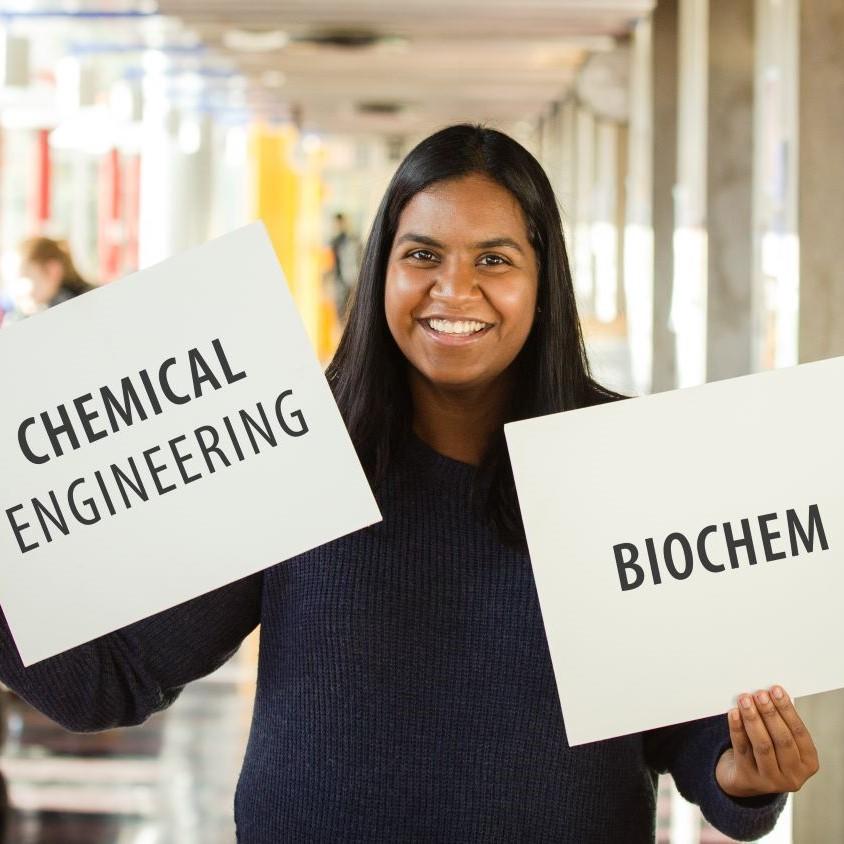 Un étudiant tient deux panneaux. L'un dit "génie chimique", l'autre "biochimie".
