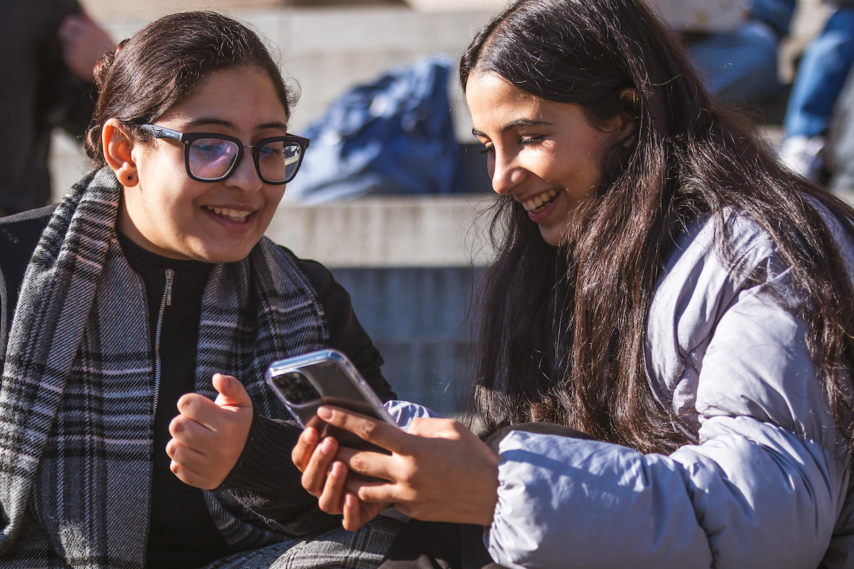 Deux étudiants discutent et regardent quelque chose sur leur téléphone.