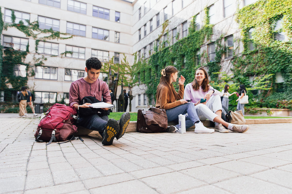 Étudiants riant sur le campus devant un mur couvert de vignes.