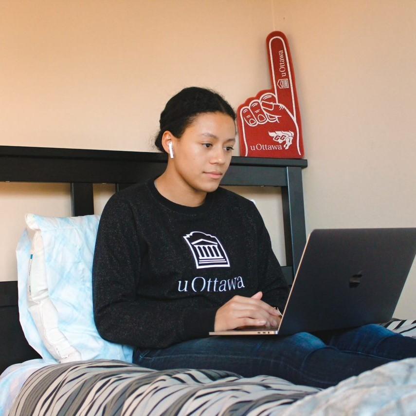 Étudiante avec un ordinateur portable assise sur un lit dans une résidence 