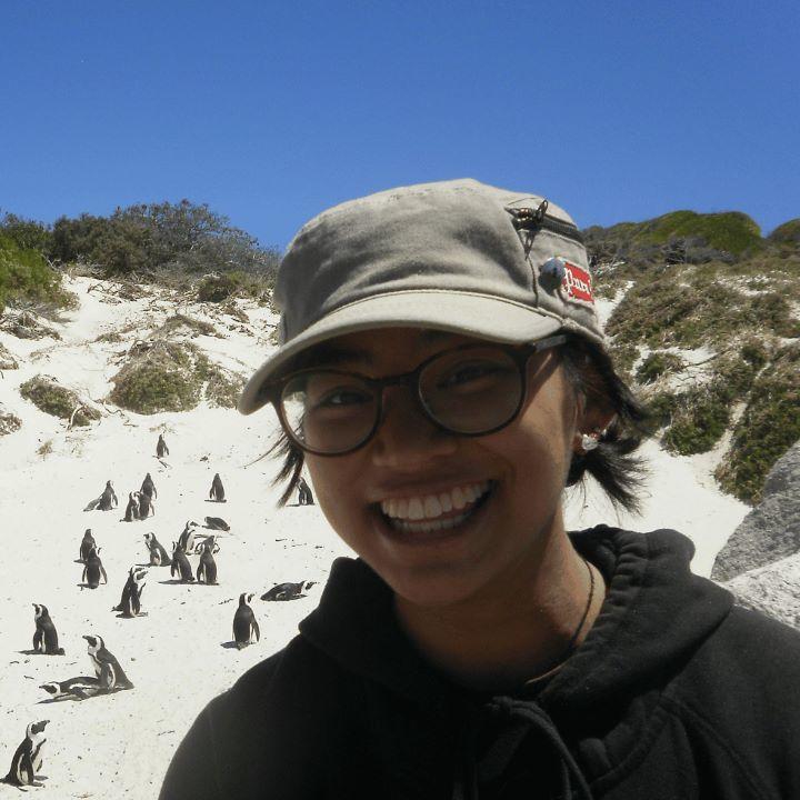 Megan Satumba sur une plage en Afrique du Sud, avec des manchots en arrière-plan.
