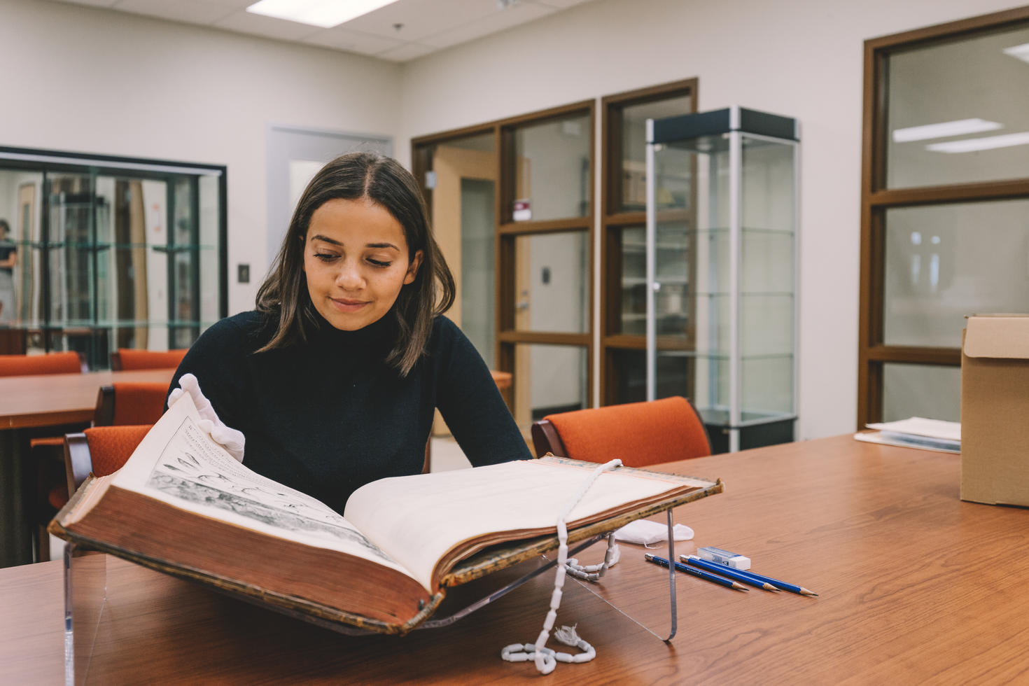 Une étudiante examine, à l'aide de gants blancs, un livre des archives.