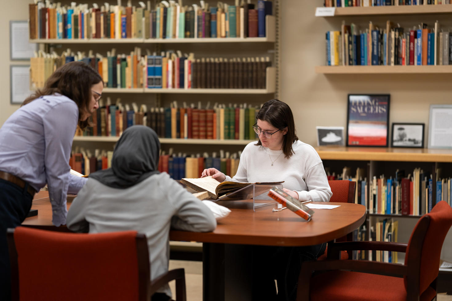 Trois étudiants étudiant autour d'un bureau, avec des étagères remplies de livres derrière eux