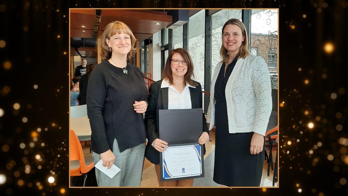 Trois femmes se tiennent face à la caméra et sourient. La femme du milieu tient un certificat.
