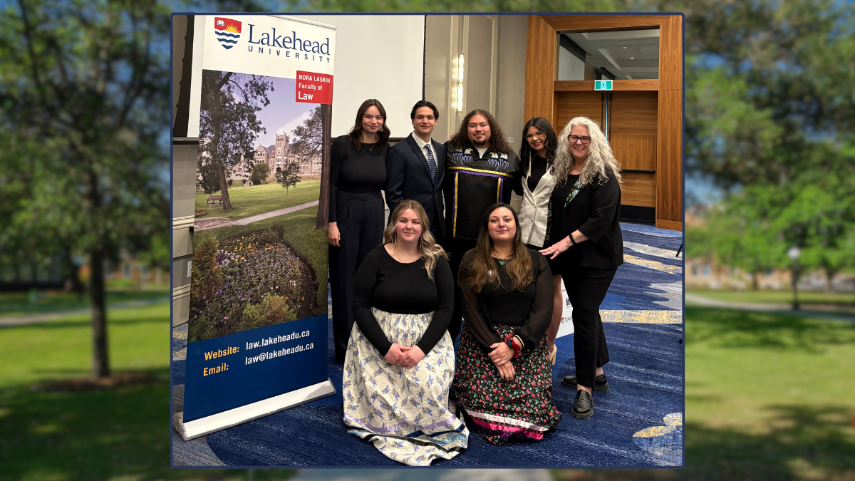 Sept personnes, dont cinq femmes et deux hommes, se tiennent debout et s'agenouillent à côté d'une banderole pour l'université Lakehead. 