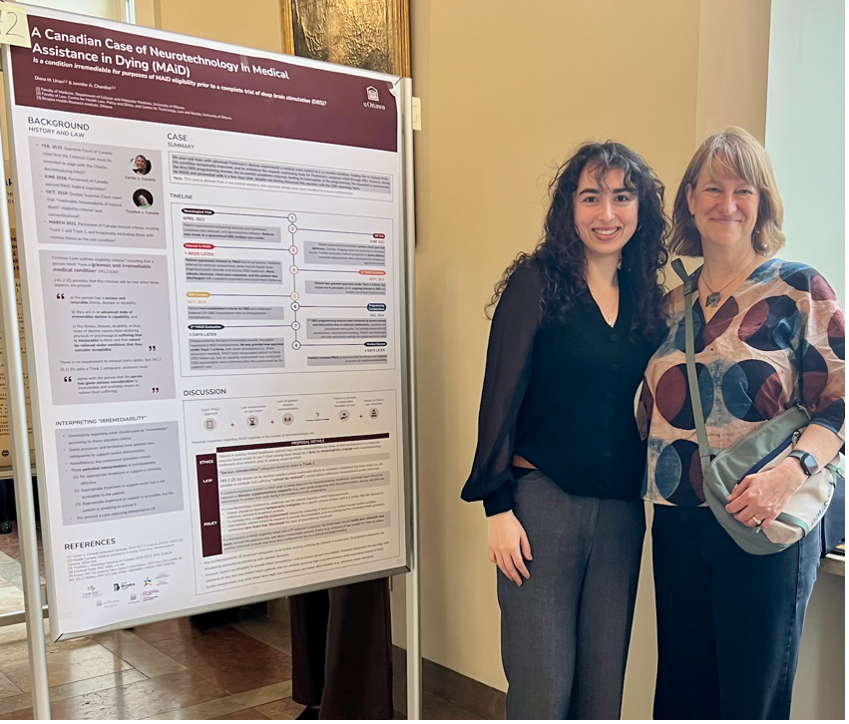 Two women stand, smiling, beside a large information panel.