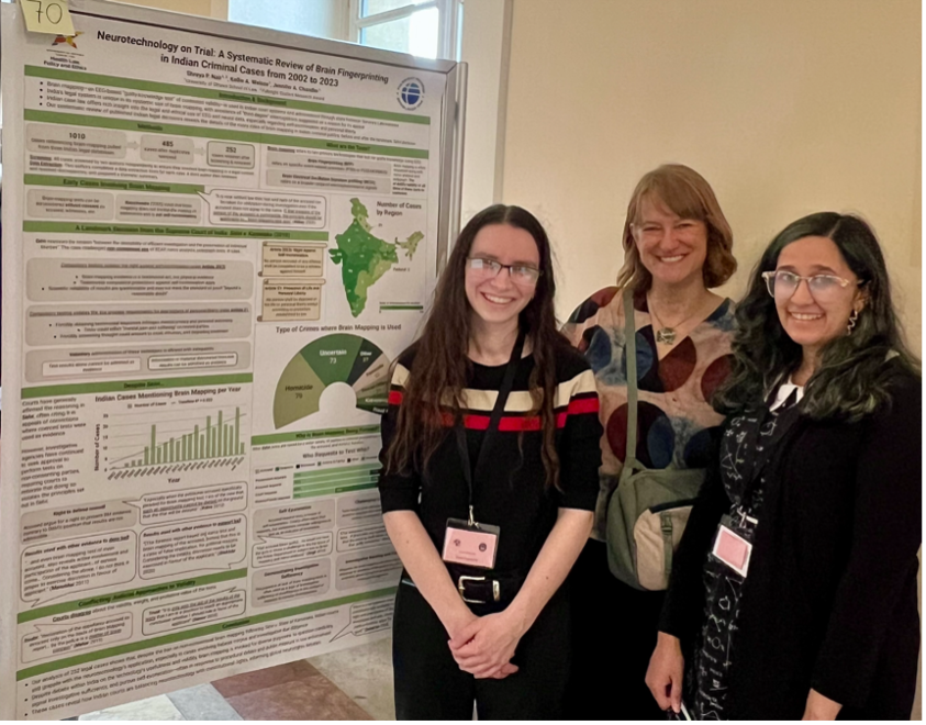 Three women stand, smiling, beside a large information panel.