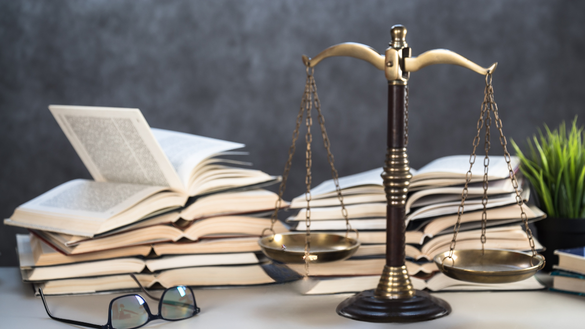 Balance de la justice avec des livres en arrière-plan et une paire de lunettes posée à sa gauche.