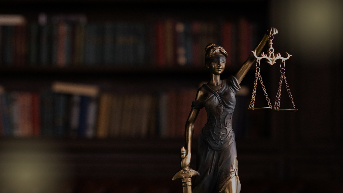 Statue of lady justice stands against a dark background of library shelves.