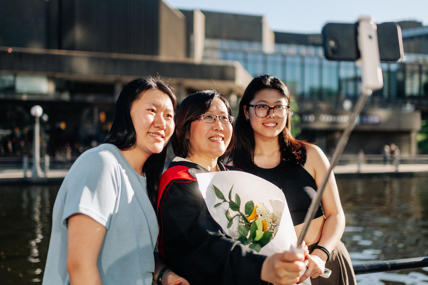 Trois femmes prennent un selfie ensemble, la diplômée au centre tenant un bouquet de fleurs.