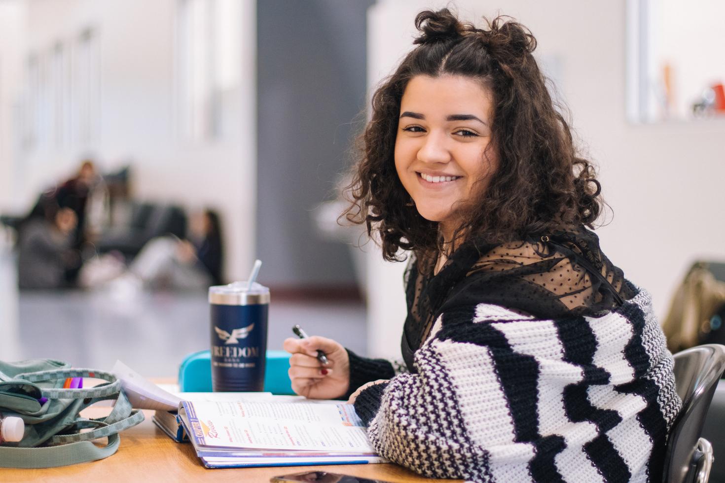 Étudiante regardant la caméra et souriant pendant qu'elle étudie.
