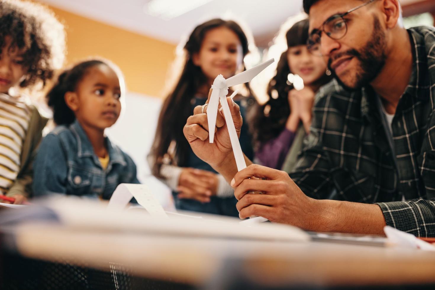 Des enfants regardent un enseignant qui brandit une éolienne en papier.