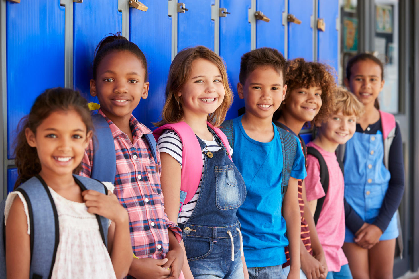 De jeunes élèves avec leurs sacs à dos devant les casiers de l'école.