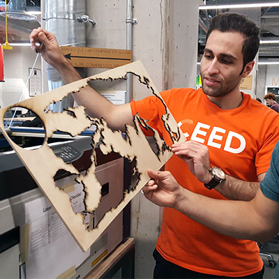 Un étudiant qui montre une oeuvre crée à l'aide d'un découpeur au laser.