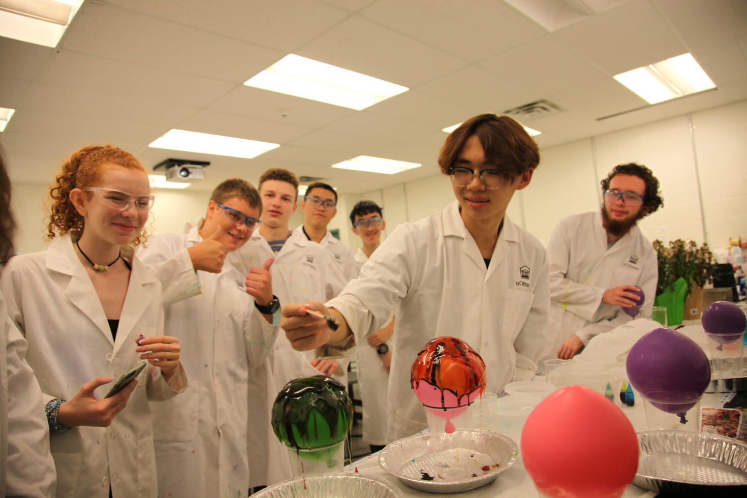 Groupe d'adolescents en blouse de laboratoire faisant une expérience scientifique avec des ballons.