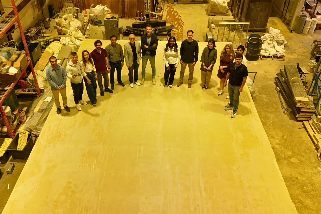 Le professeur Doudak avec un groupe de ses étudiantes et étudiants aux cycles supérieurs et un collaborateur de recherche, debout en demi-cercle à l'intérieur d'un grand atelier industriel, vu d'en haut.
