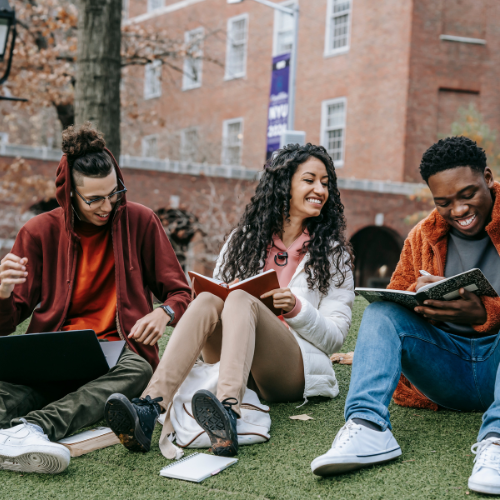 Trois étudiants assis sur l'herbe, souriants.