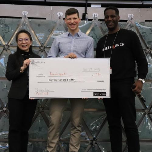 Un étudiant heureux posant avec la doyenne de la Faculté de génie, tenant un grand chèque adressé à son entreprise.