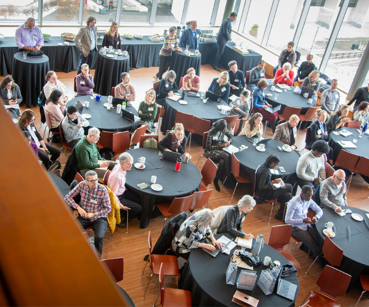 Une foule de personnes assises autour de tables de conférence, vue d'en haut.