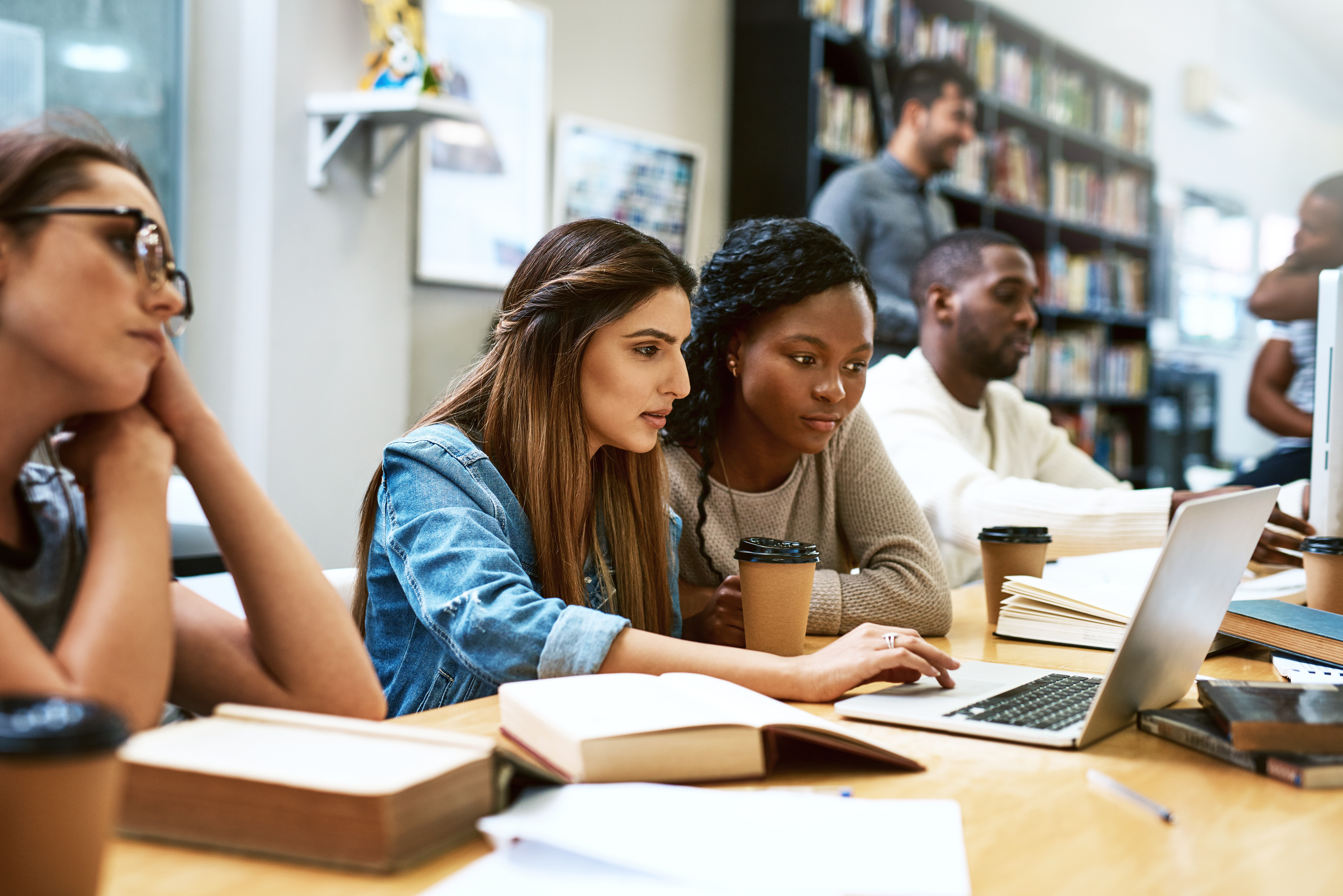 Personnes travaillant sur des ordinateurs portables et prenant des notes dans une bibliothèque ou un espace d’apprentissage.