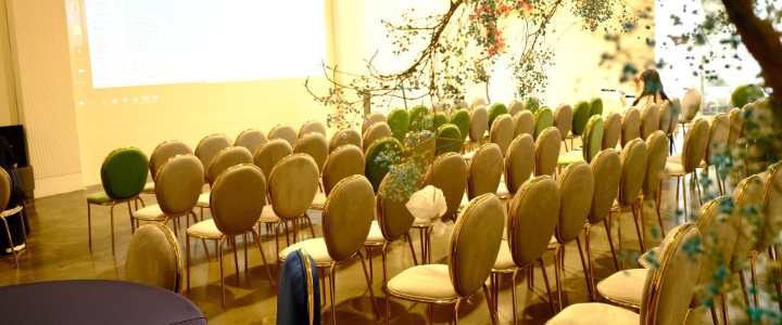 Des rangées de chaises face à une présentation avec une table et un arbre en surplomb.