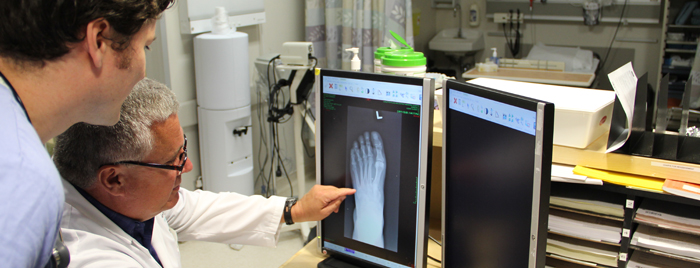 Un précepteur explique quelque chose à un étudiant, à propos d'une photo radiographique d'un pied sur un écran d'ordinateur.