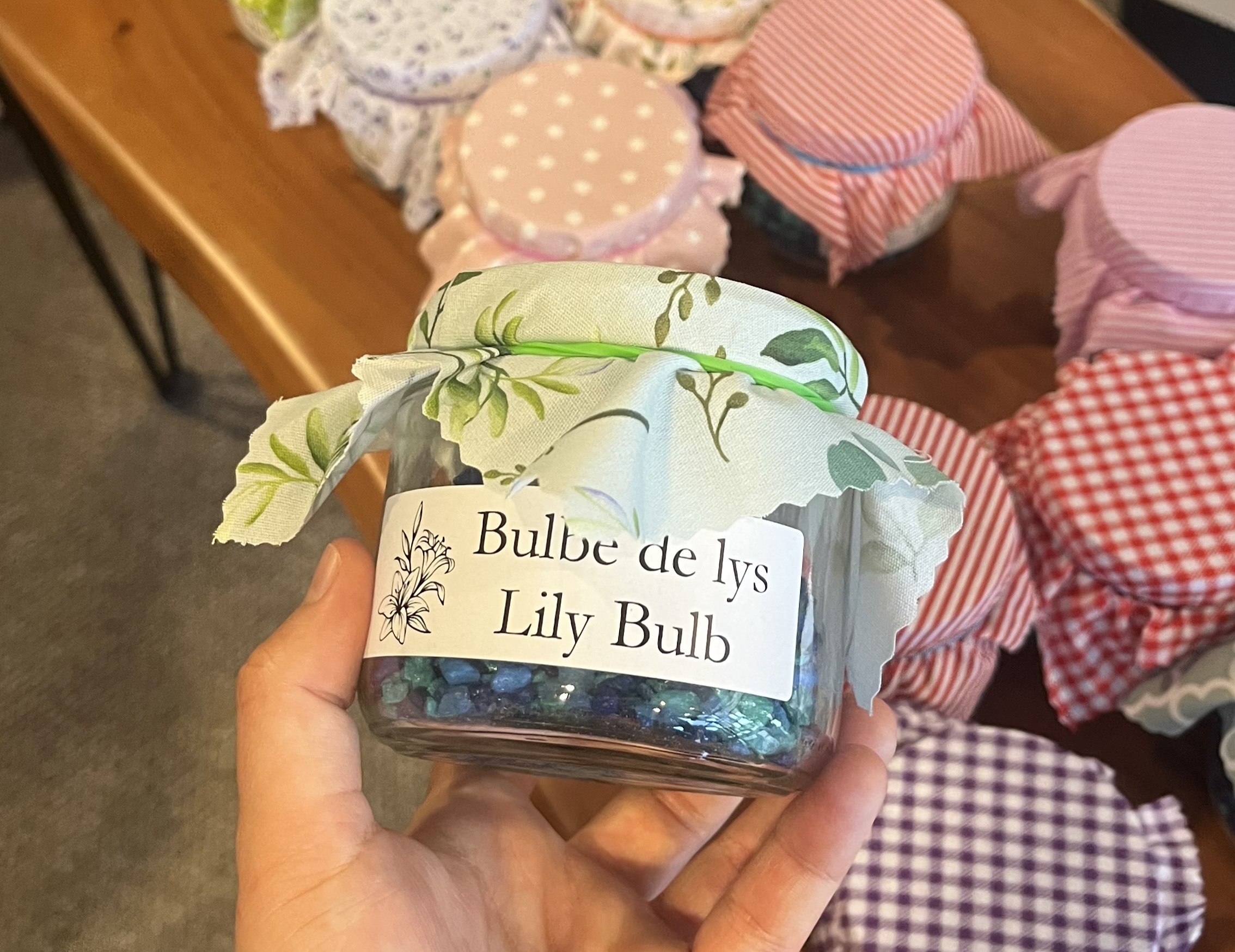 Des bulbes de lys et des petits cailloux dans un bocal en verre avec une étiquette et un couvercle en tissu, tenu par un membre du personnel.