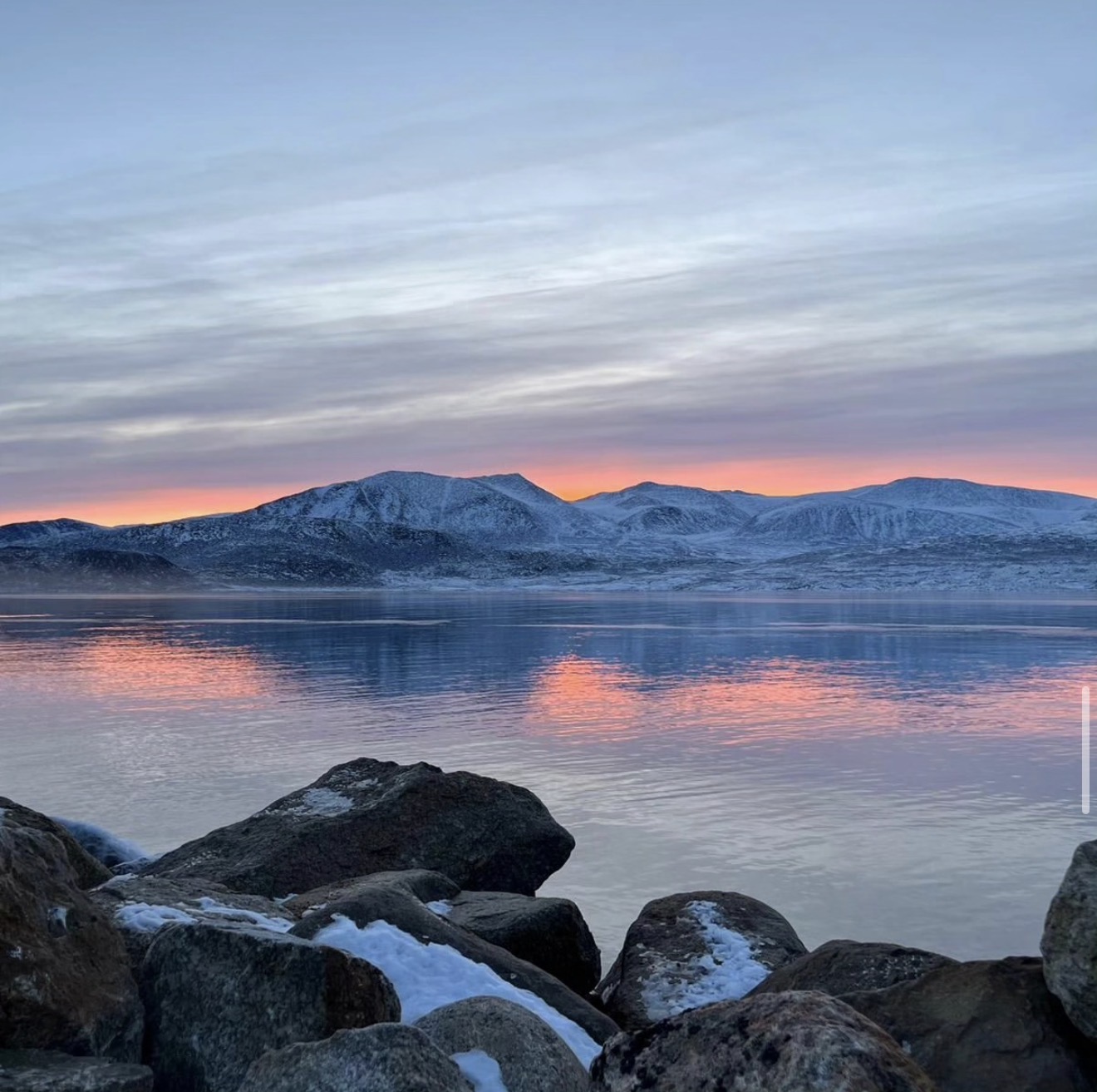 A sunrise over Nunavut waterfront featuring snow-capped mountains in the background and pink and purple skies