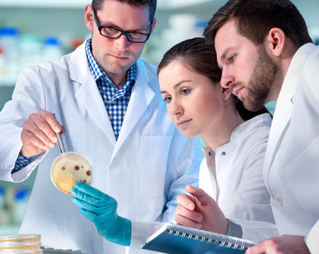 Scientifiques, deux hommes, une femme, portant des blouses blanches et travaillant au laboratoire.