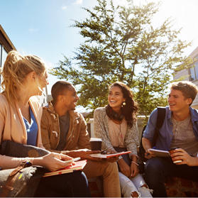 Quatre étudiants assis dehors au soleil, parlant et riant.