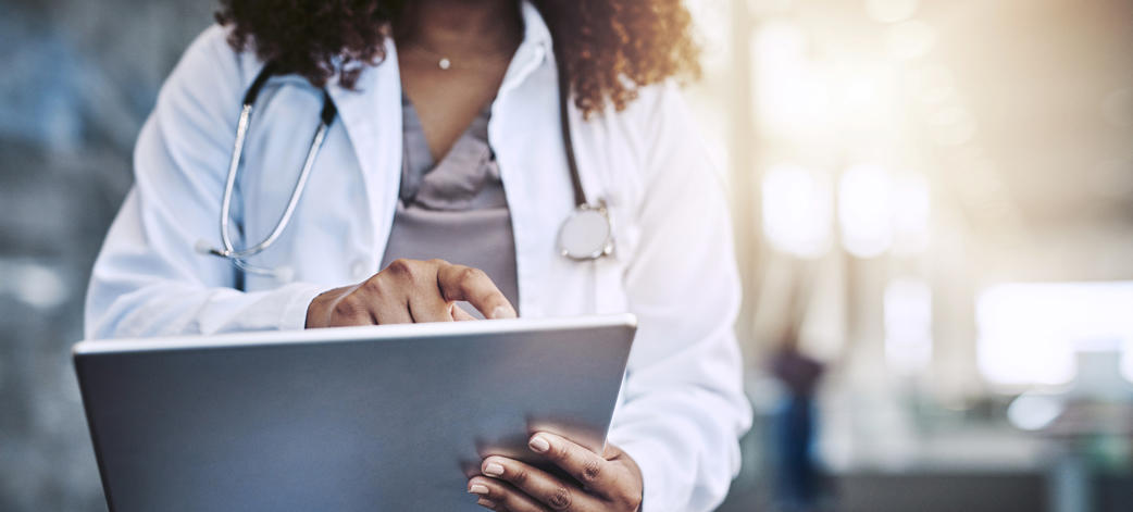 Un médecin en blouse blanche utilise une tablette, concentré sur l'écran. 