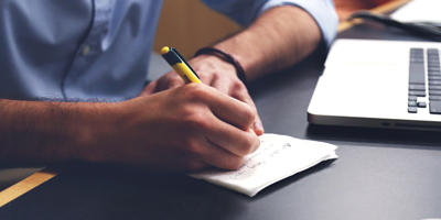 Un homme assis devant un ordinateur prend des notes sur un papier