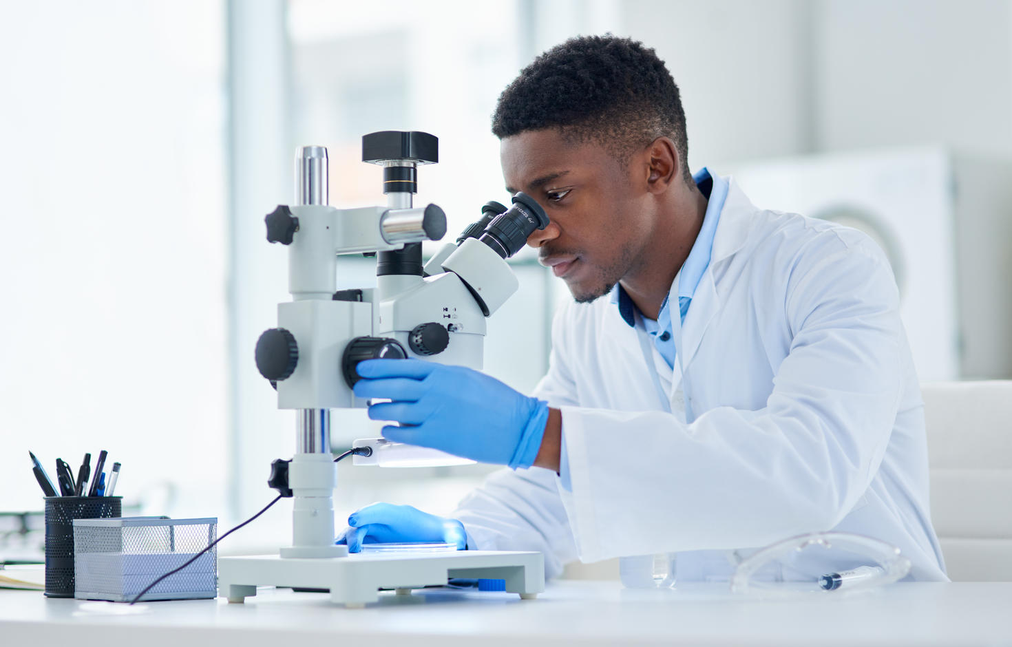 Plan recadré d'un jeune scientifique concentré regardant des échantillons de test à travers un microscope à l'intérieur d'un laboratoire pendant la journée.