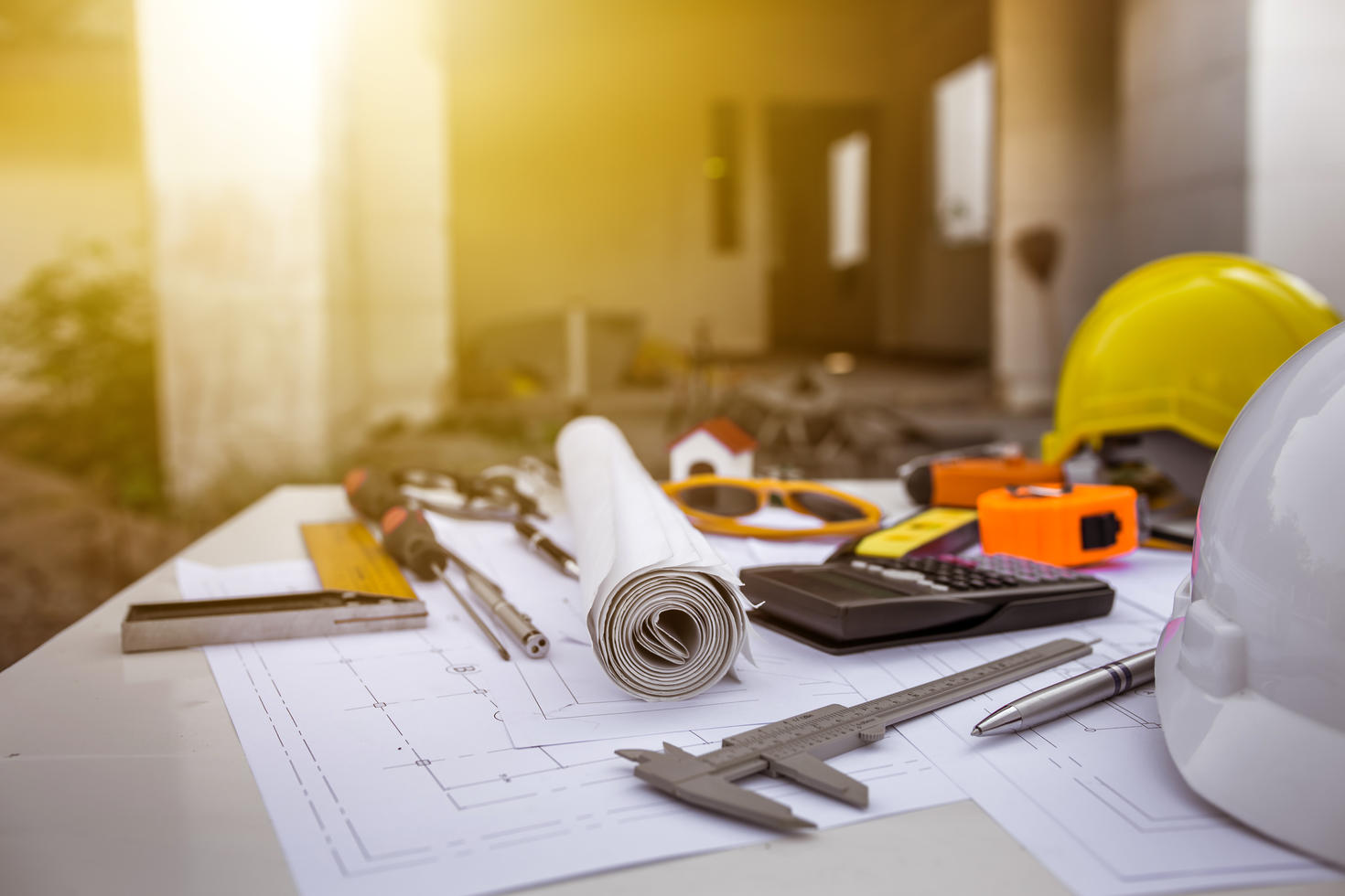 Plans architecturaux sur une table avec des outils de construction, des casques de sécurité et des instruments de mesure sur un chantier