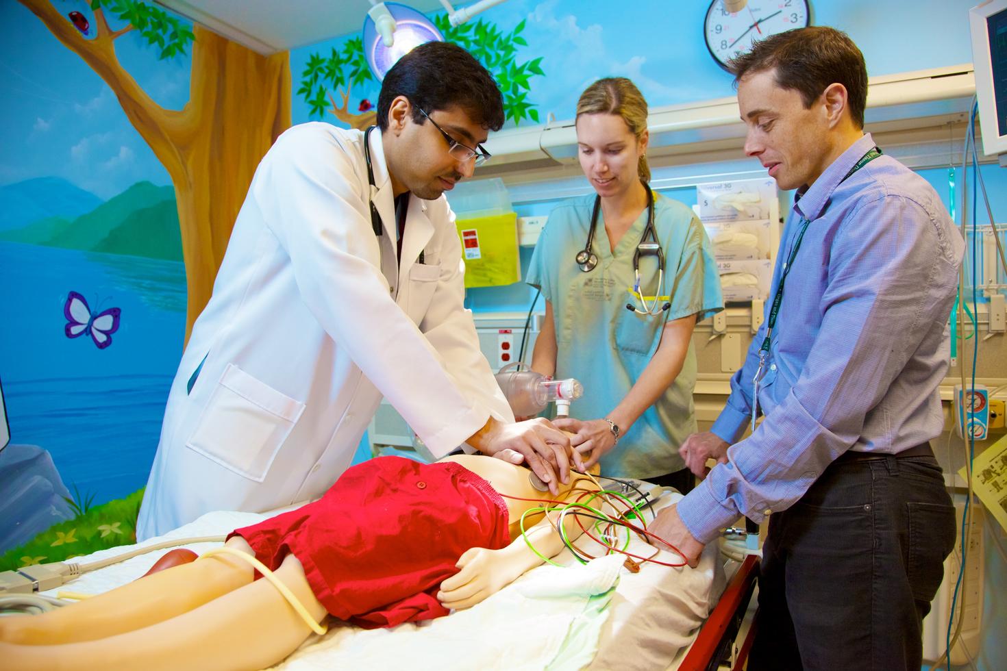 Des résidents s'entraînent à pratiquer la réanimation cardio-pulmonaire sur un mannequin pendant que le médecin de l'équipe leur fait part de ses commentaires.