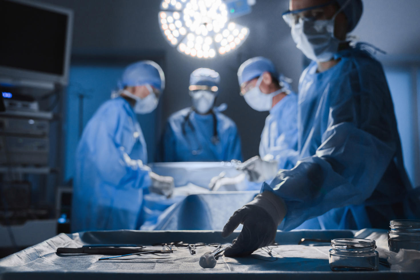 Outils chirurgicaux posés sur une table tandis qu'un groupe de chirurgiens à l'arrière-plan opère un patient dans une salle d'opération.