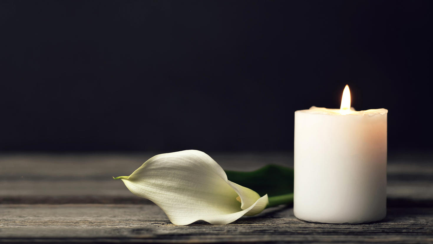 une bougie blanche et un pétale de rose blanc posés sur une table avec un fond sombre