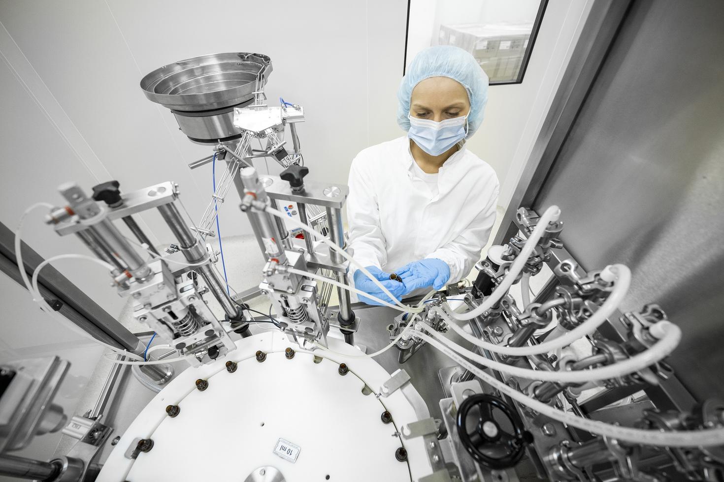 Des petits flacons bruns sont parfaitement disposés dans un laboratoire pendant la fabrication dans une usine pharmaceutique, tandis qu'un employé contrôle le processus.
