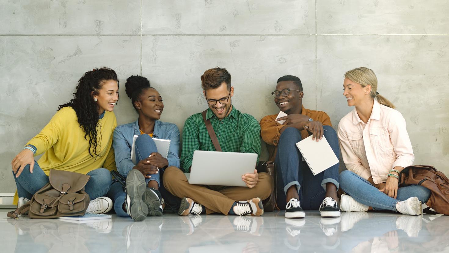 Des étudiants universitaires heureux utilisent un ordinateur portable alors qu'ils sont assis dans un couloir.