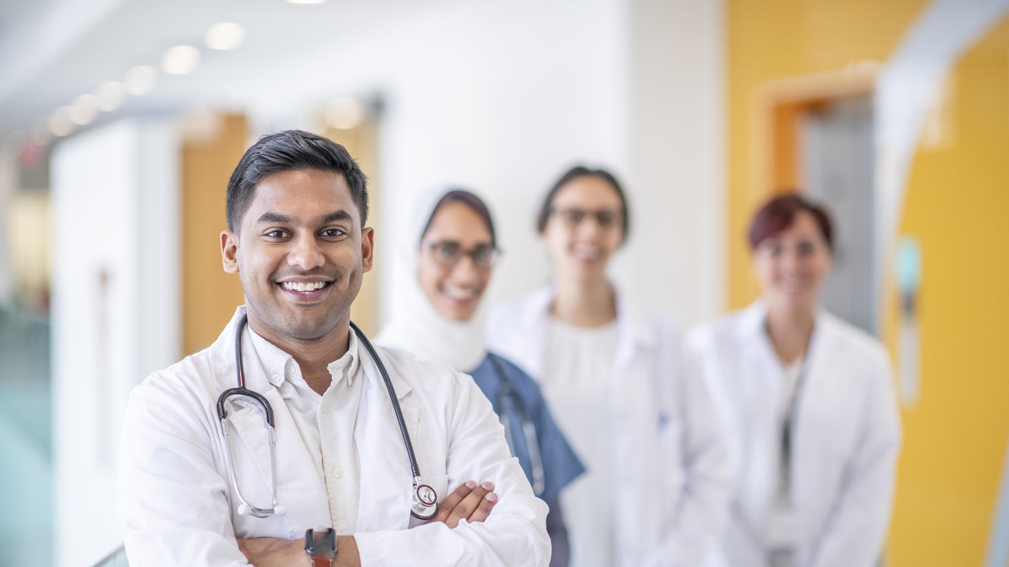 Un médecin se tient debout avec son équipe médicale derrière lui à l'intérieur d'un bâtiment hospitalier.