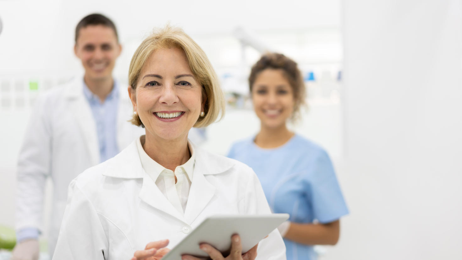 Portrait d'un dentiste heureux au cabinet avec son équipe et tenant une tablette informatique